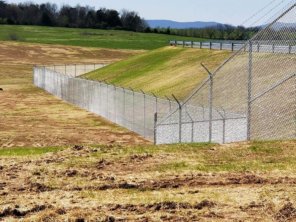 A chain link fence surrounds a field with mountains in the background