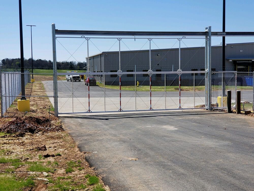 A sliding gate is open to a parking lot with a building in the background