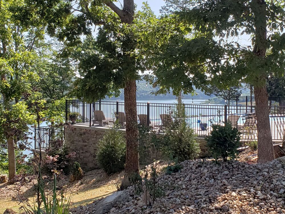 A view of a lake through a fence surrounded by trees and rocks.