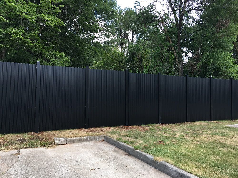 A black fence is surrounded by trees and grass in a yard.