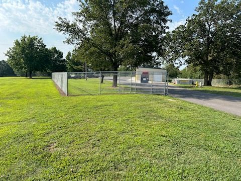 A large grassy field with a fence and trees in the background.