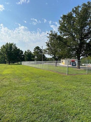 A large grassy field with a fence and trees in the background.
