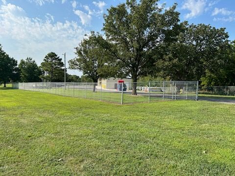 A large grassy field with a fence and trees in the background.