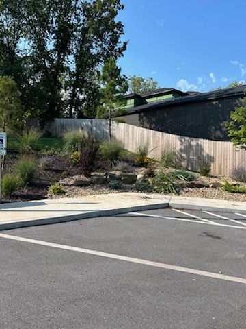 A parking lot with a wooden fence and a house in the background.