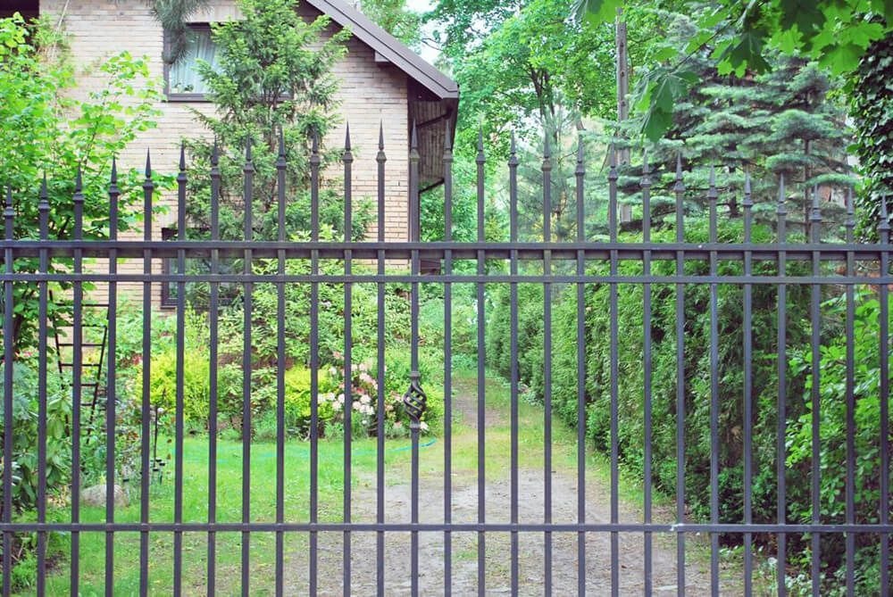 A wrought iron fence surrounds a driveway leading to a house.