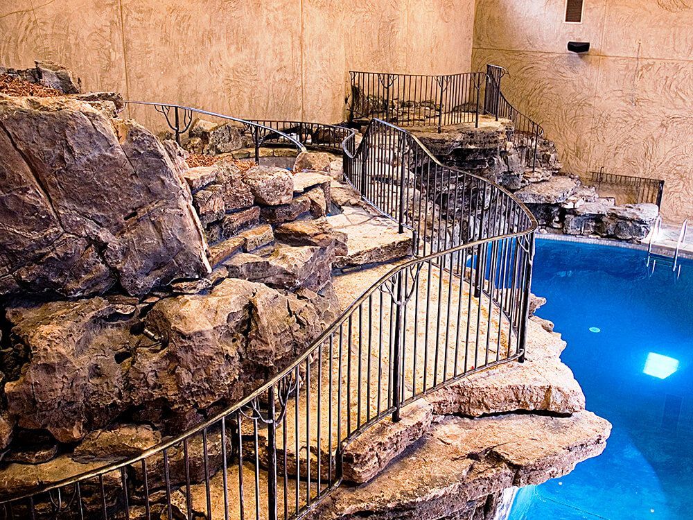 A large swimming pool surrounded by rocks and a metal fence done by best fencing company in Springfield MO