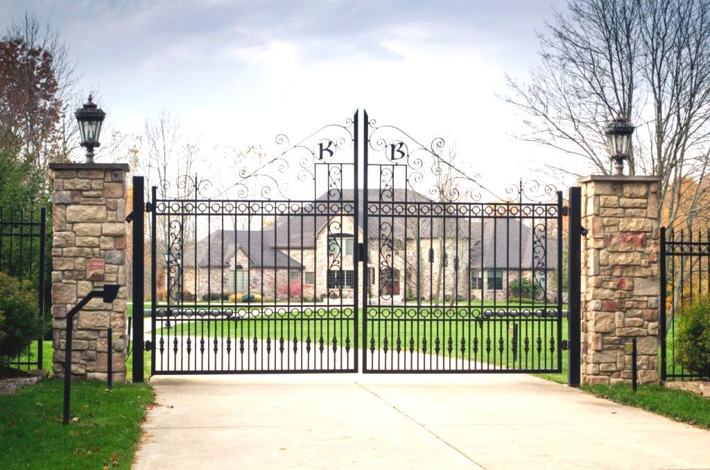 A wrought iron gate is open to a driveway leading to a house | installation by fencing company in Springfield, Ozark, MO