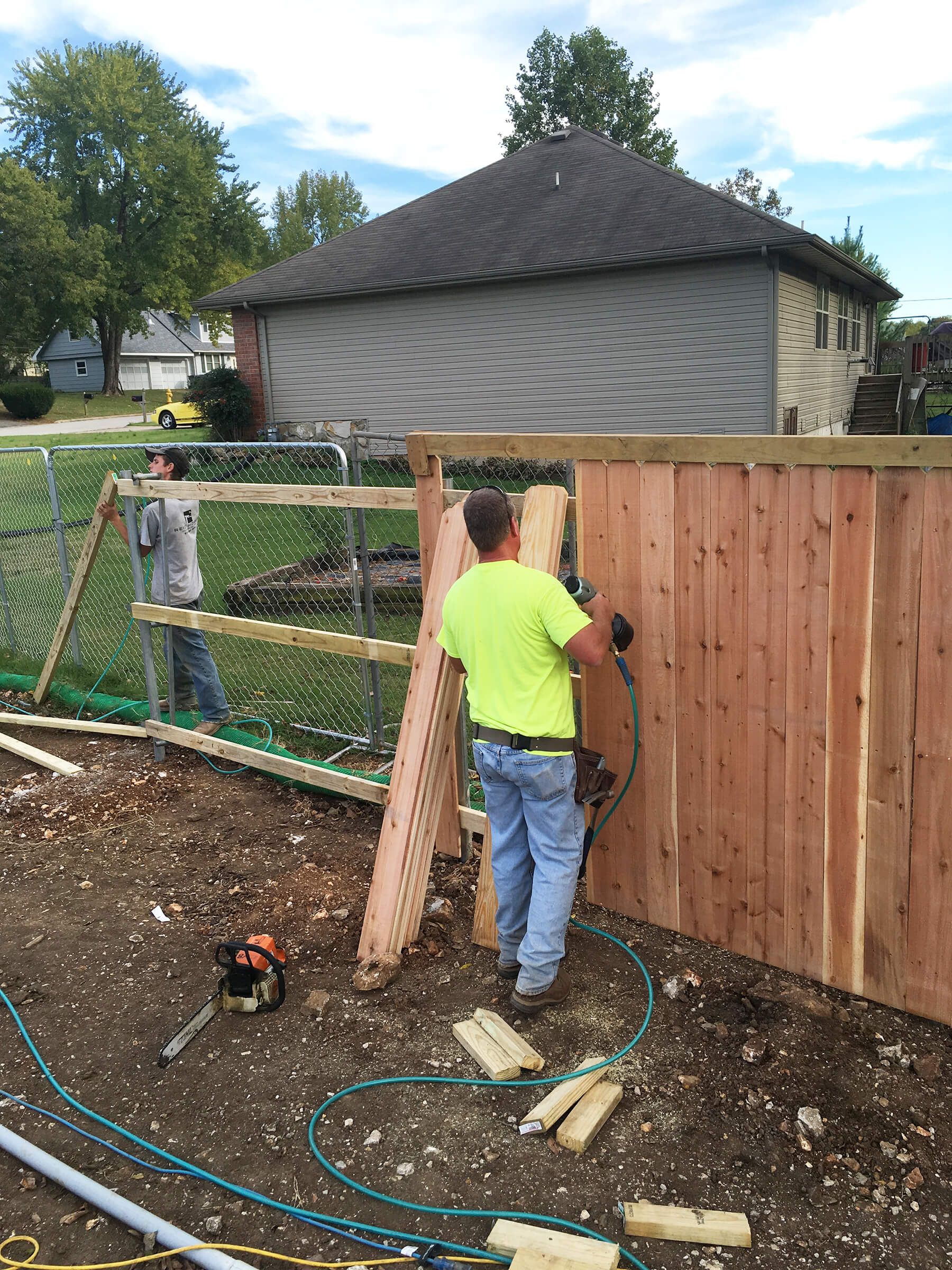 A man is working on a wooden fence in front of a house.