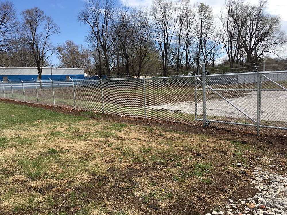 A chain link fence surrounds a grassy field with trees in the background.