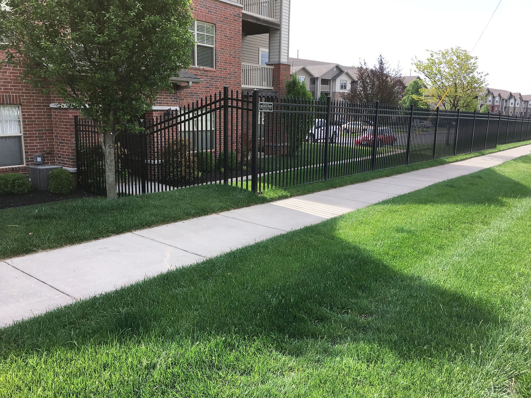 A fence surrounds a lush green lawn next to a sidewalk.