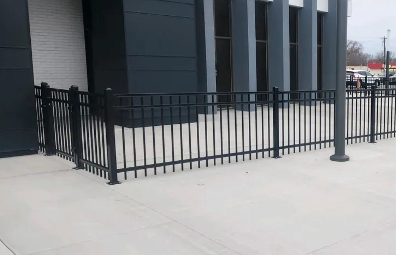 A black metal fence is surrounding a sidewalk in front of a building.