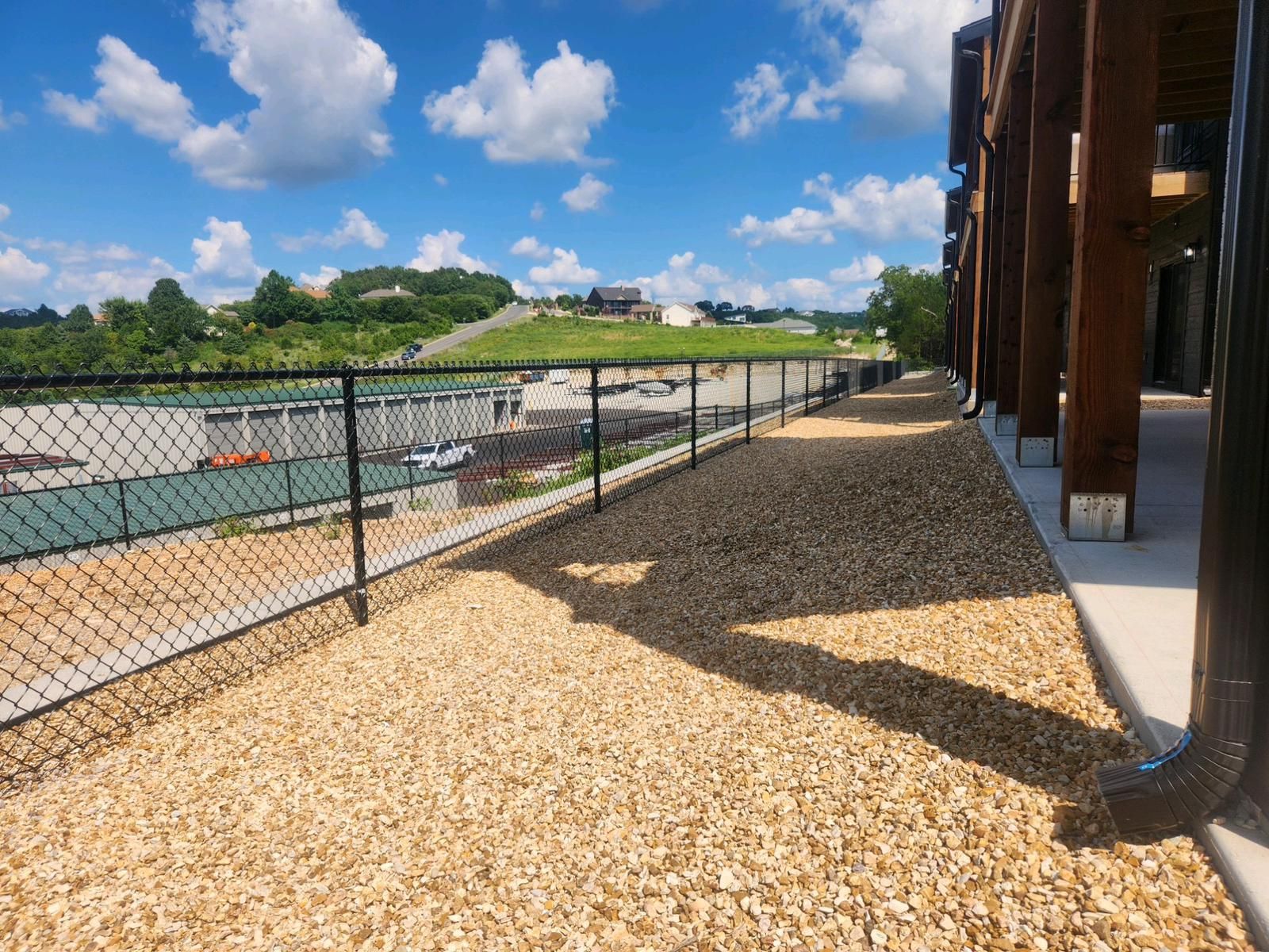 A chain link fence surrounds a gravel path leading to a building.