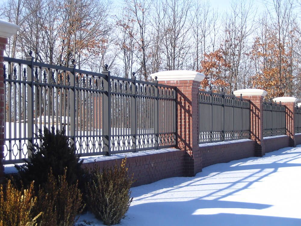 A snowy fence with a brick wall and trees in the background