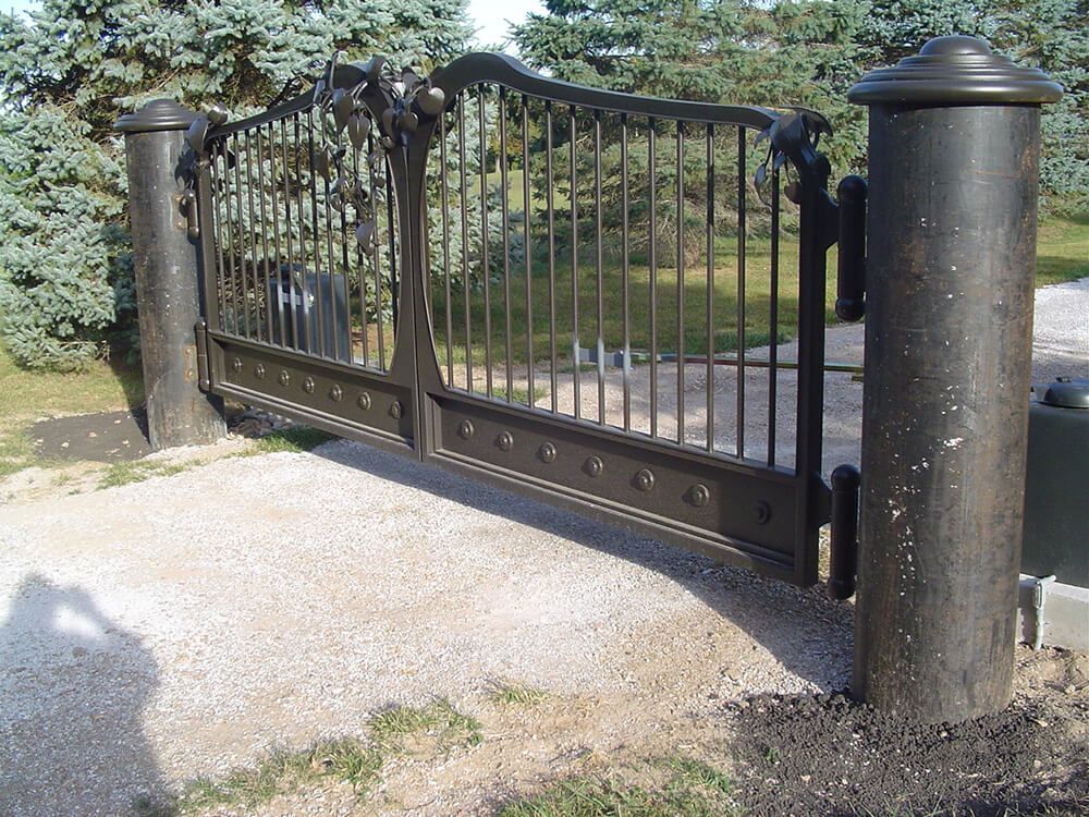 A wrought iron gate is open to a gravel driveway