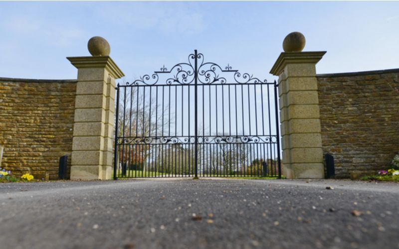 A wrought iron gate is open to a driveway.