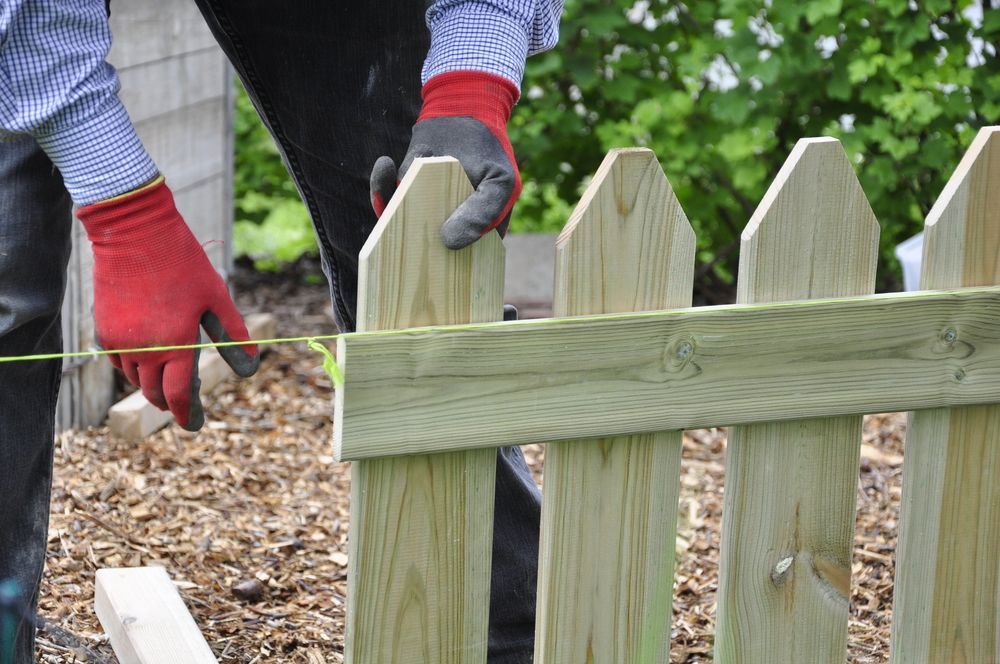 A man is measuring a wooden fence with a tape measure.