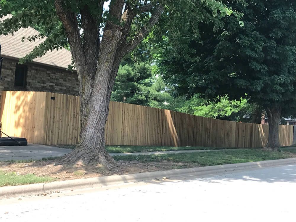 A wooden fence is surrounded by trees on the side of the road.