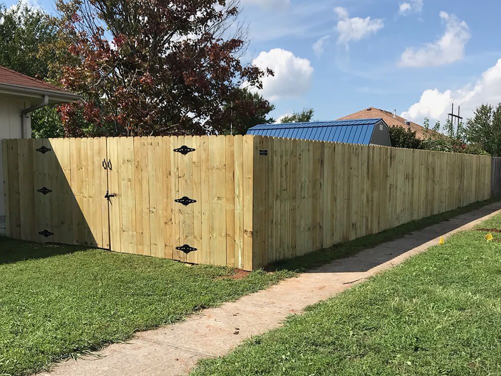 A wooden fence is sitting next to a sidewalk in front of a house.