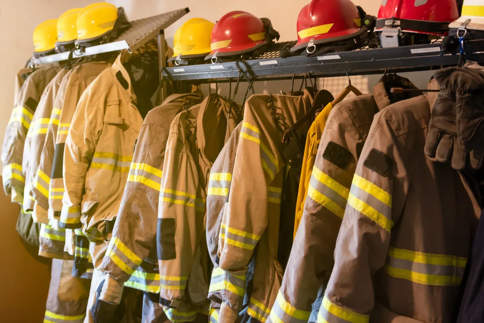 A row of firefighter 's uniforms and helmets hanging on a rack.