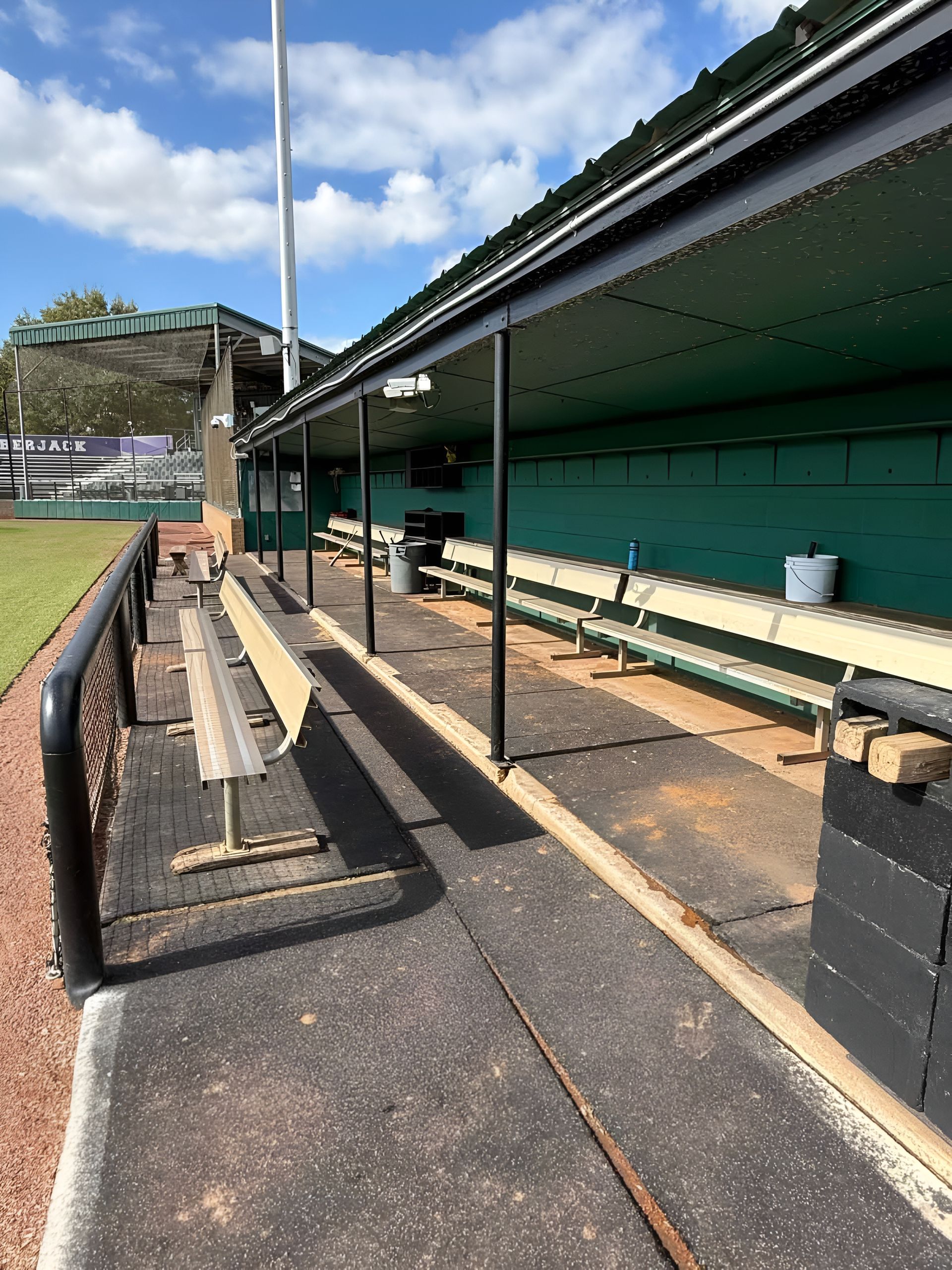 Empty sports dugout with wooden benches and green roof beside a field on a sunny day