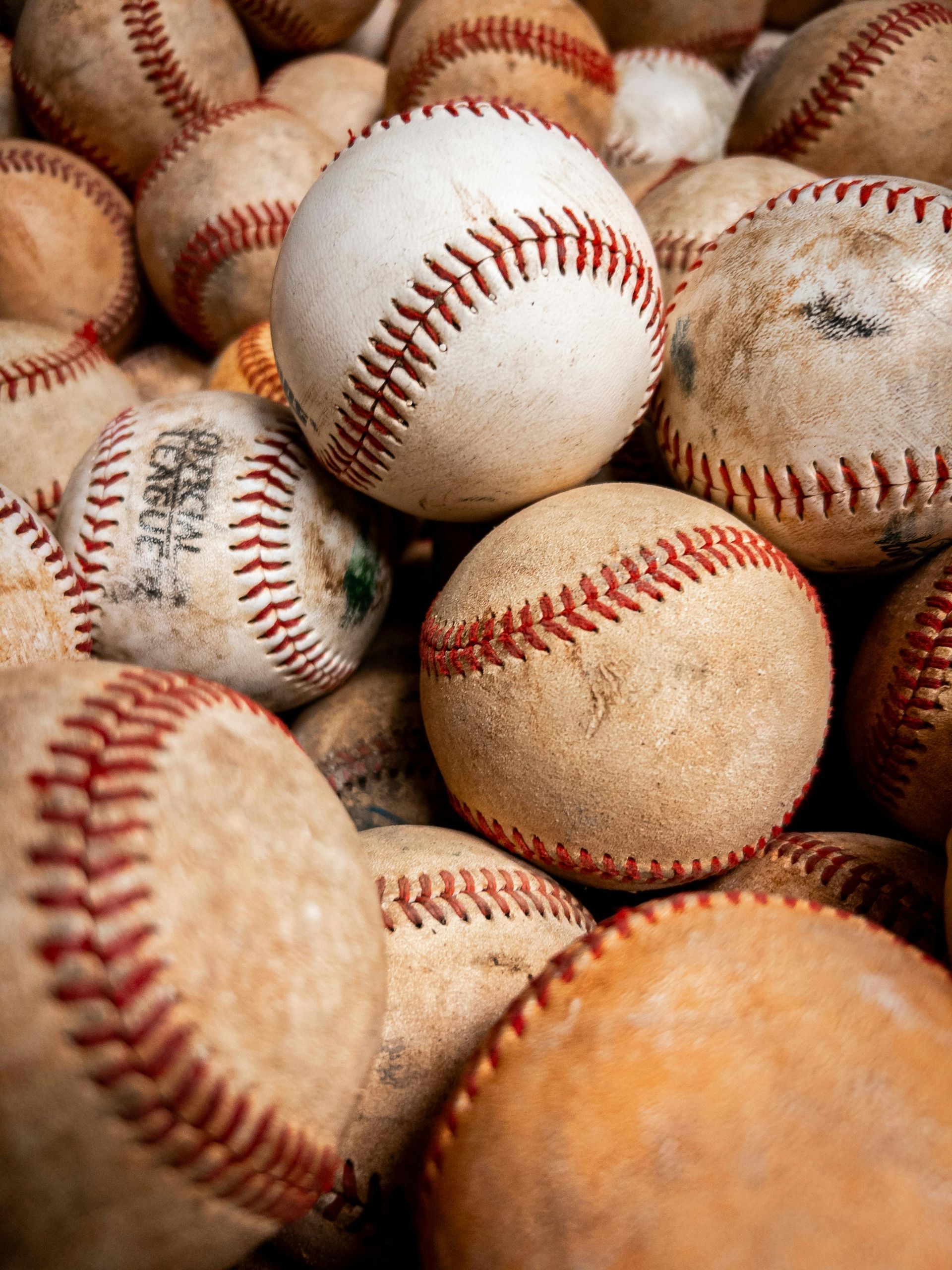 Pile of worn baseballs with red stitching in a close-up view