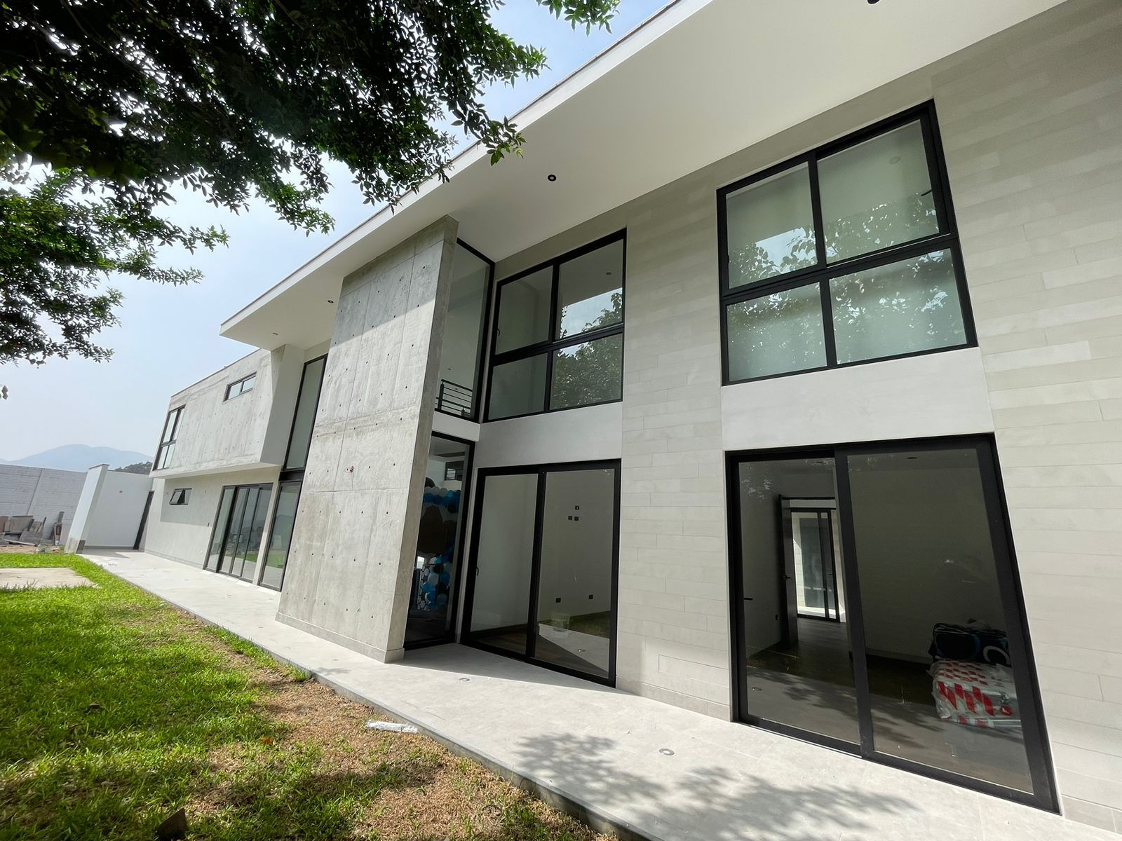 Moderna casa de dos pisos con grandes ventanales, fachada de hormigón y césped verde.