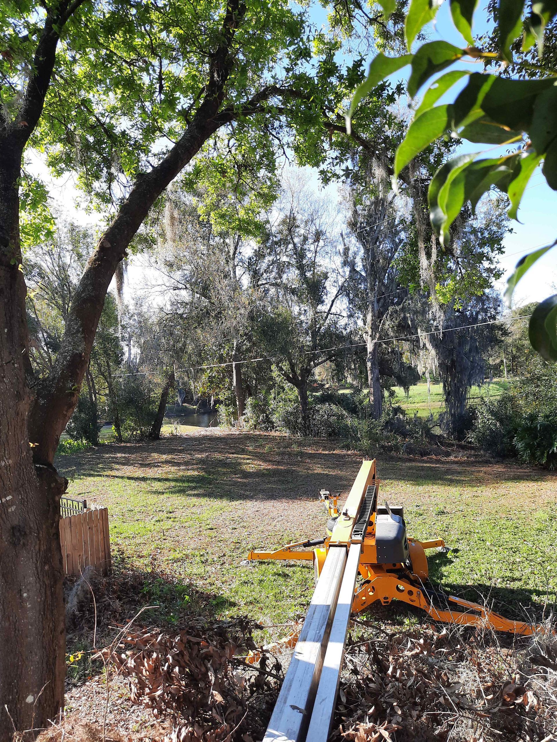 A yellow lift truck positioned in a grassy yard, trees in the background under a blue sky.