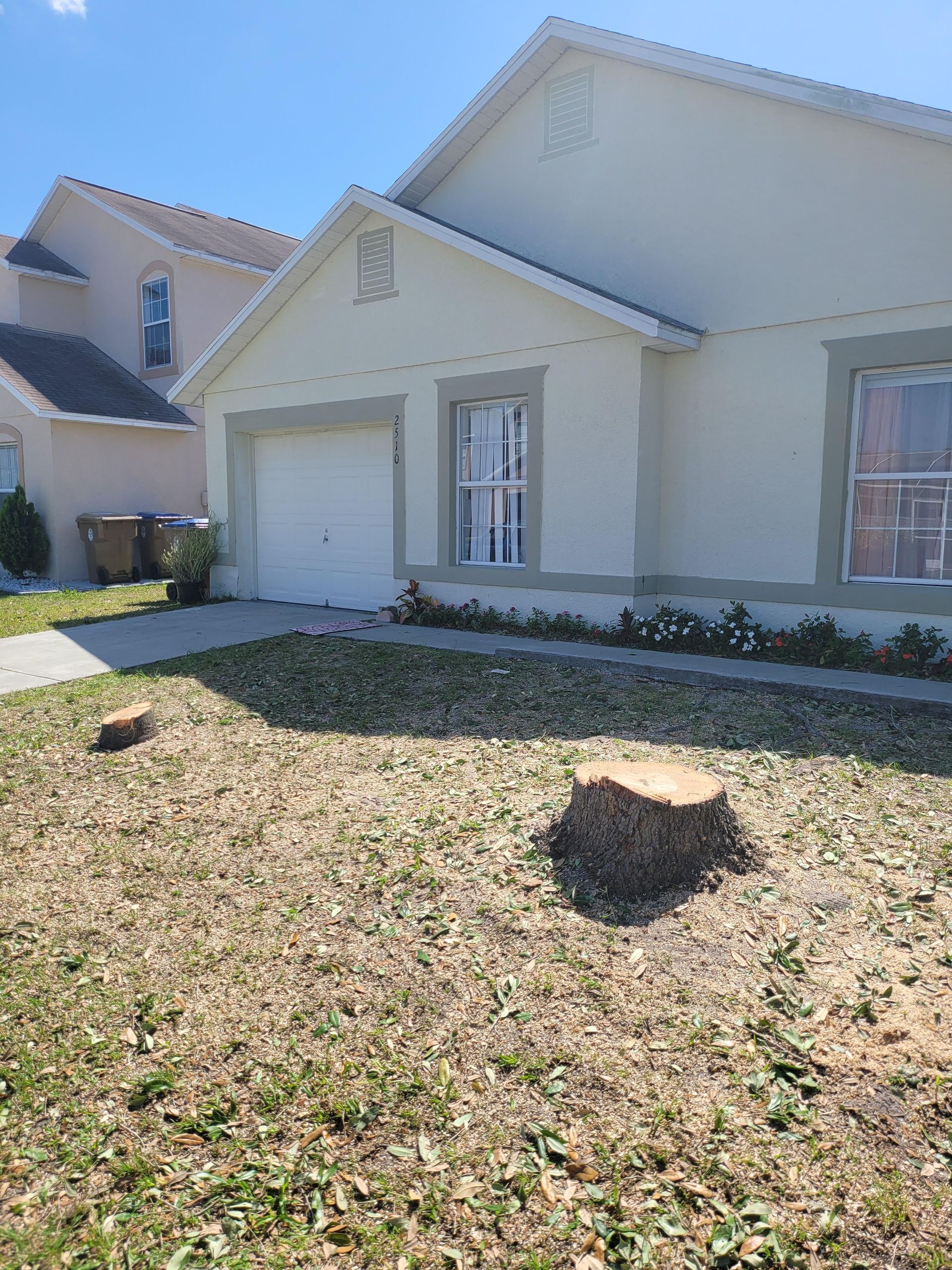 A house with a white exterior and a front lawn with two tree stumps.