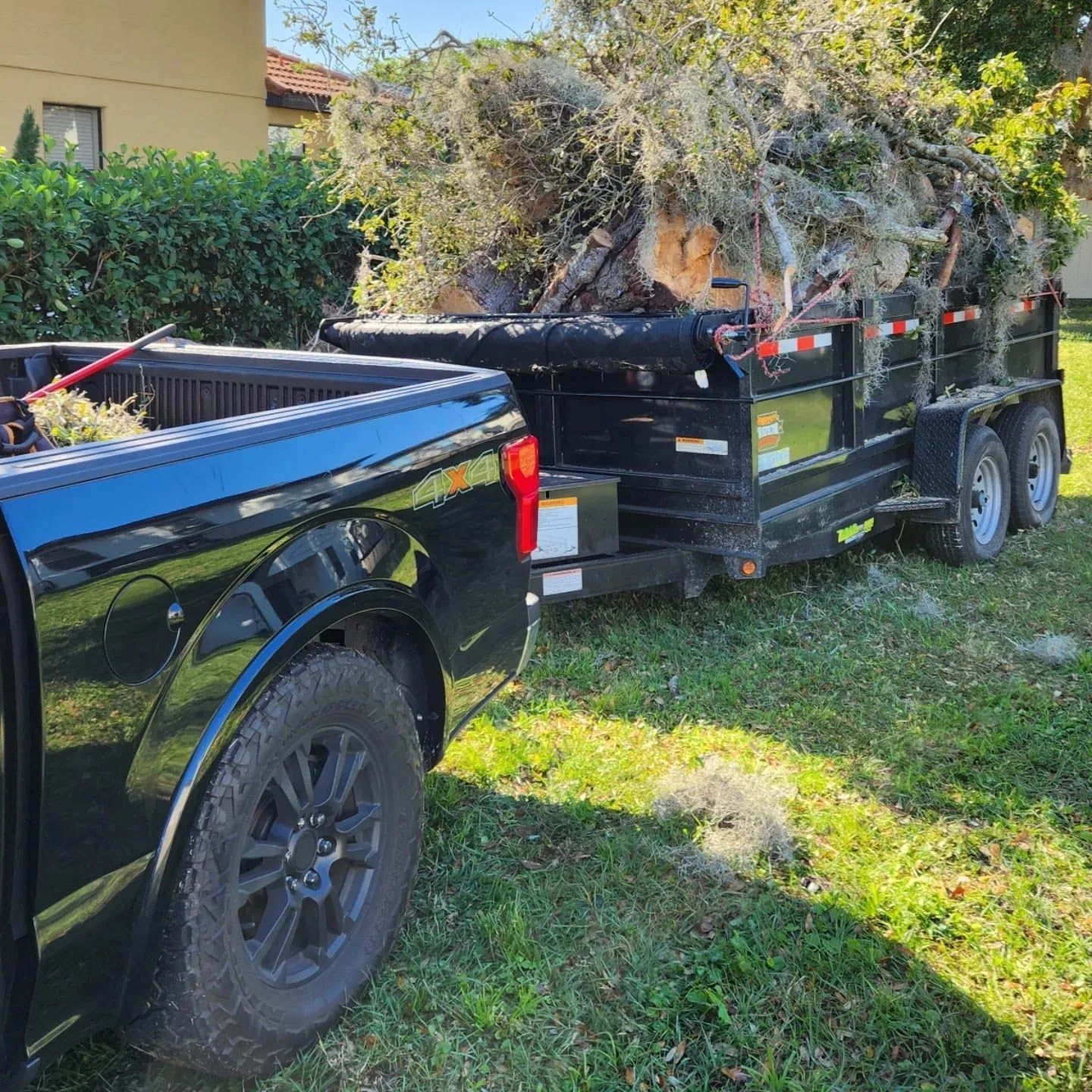 Black truck towing a black trailer filled with tree branches on a grassy lawn.