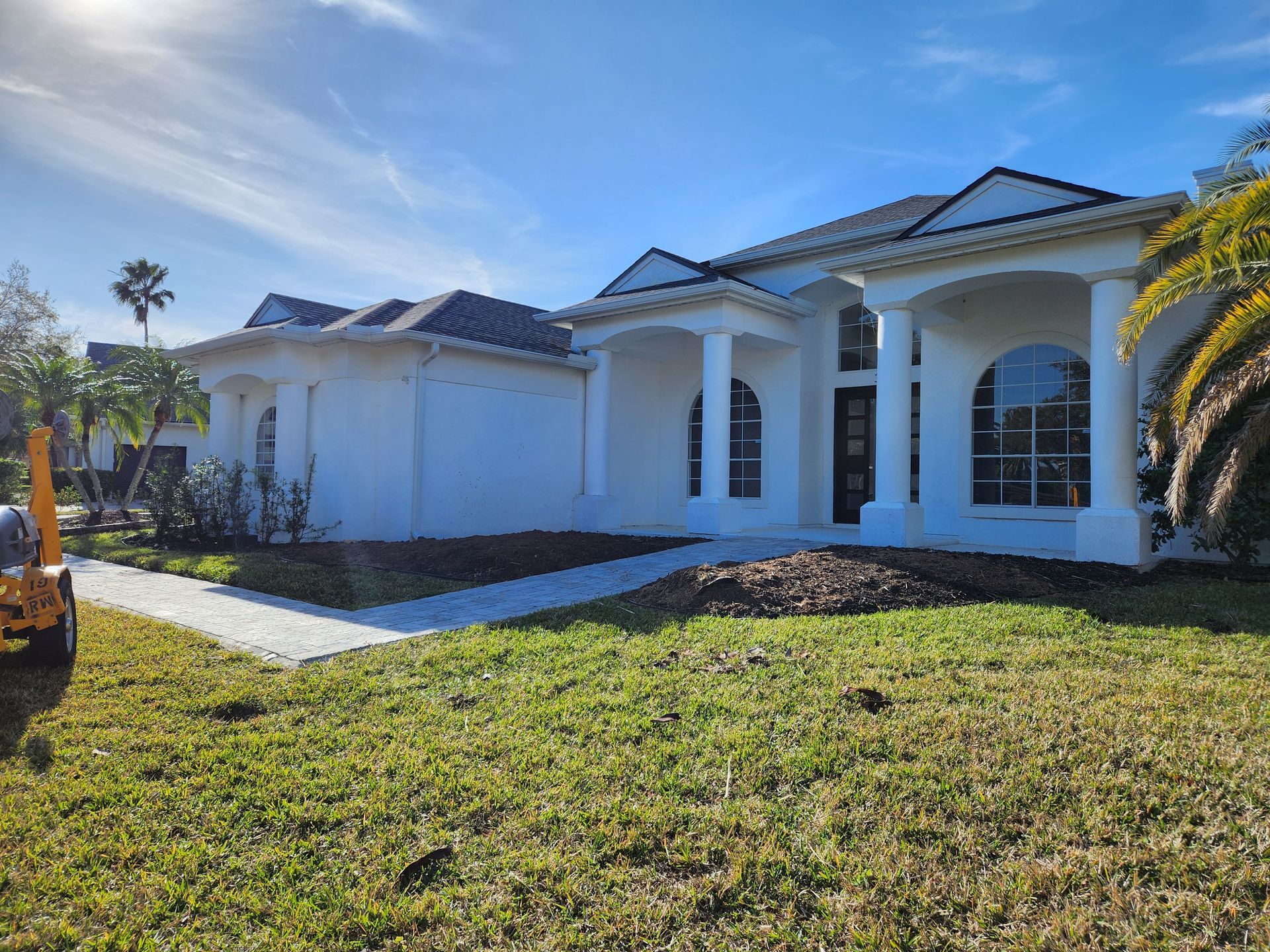 White stucco house with pillars, arched windows, and dark roof under a blue sky.