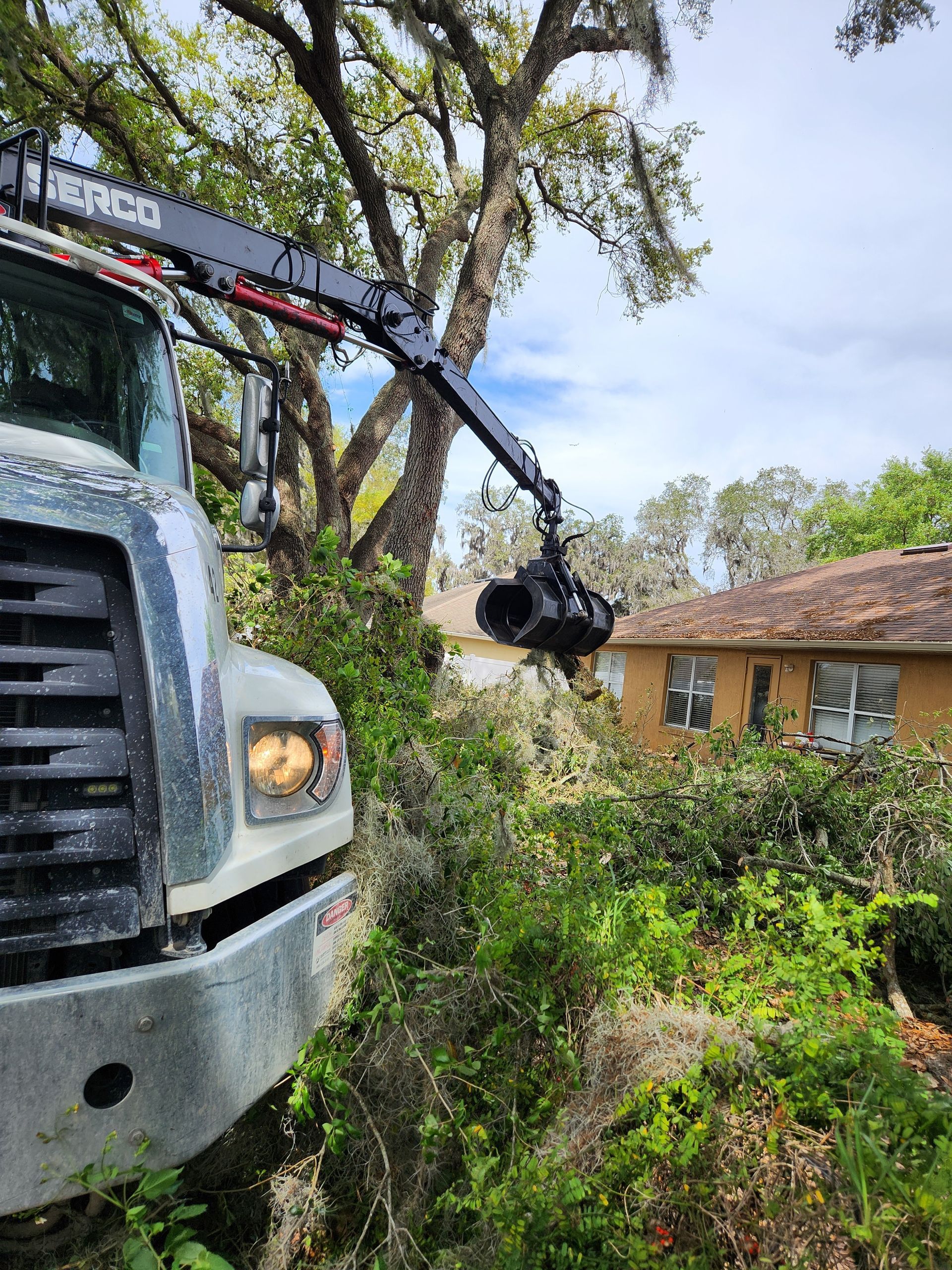 Truck with a camera crane filming a house surrounded by greenery on a cloudy day.