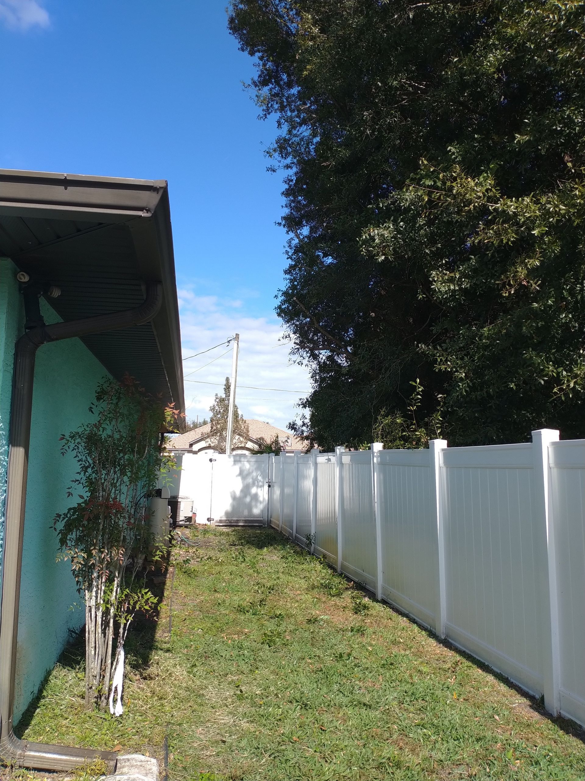 Side view of a turquoise house, a white fence, and a grassy area under a bright blue sky.