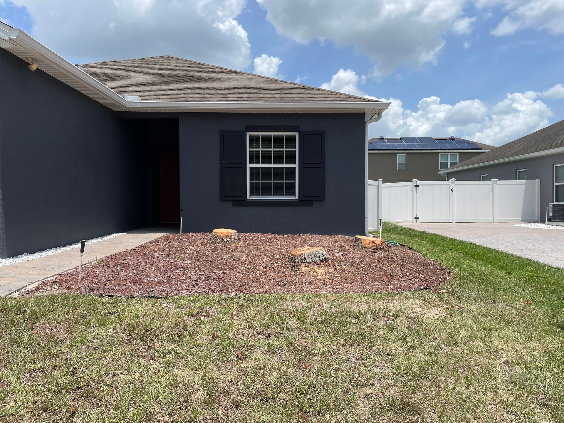 Dark blue house exterior with a white window and black shutters. Reddish mulch and green lawn.