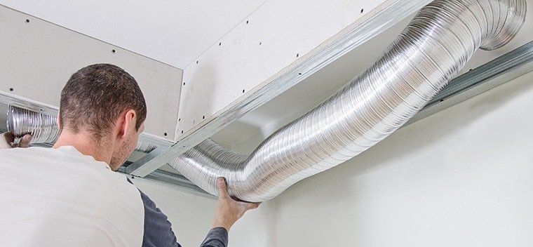 Worker installing silver ductwork in a commercial building, securing the ducts with metal brackets.