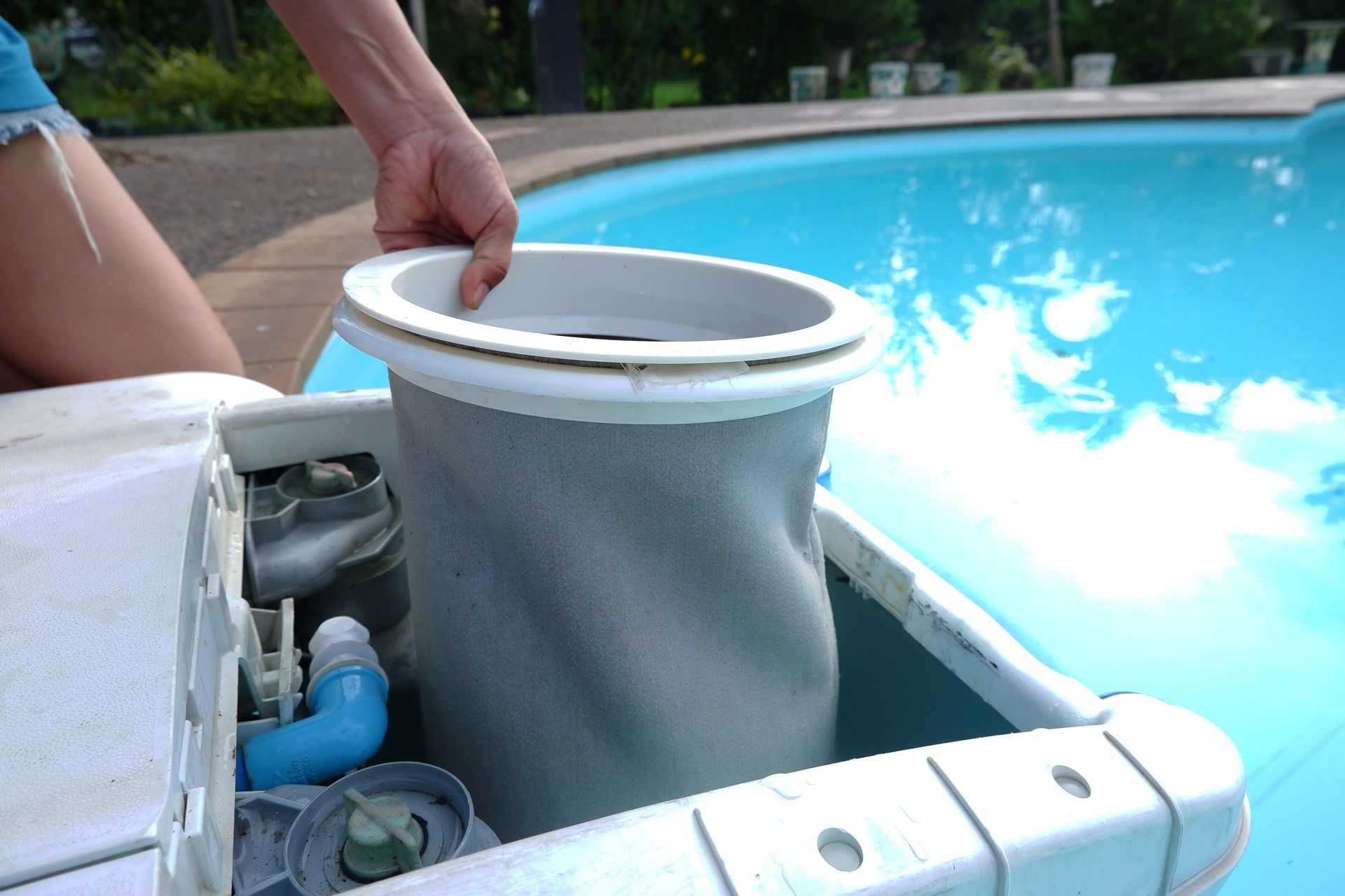 Female hand carefully pulling out the filter bag from the swimming pool filtration system.