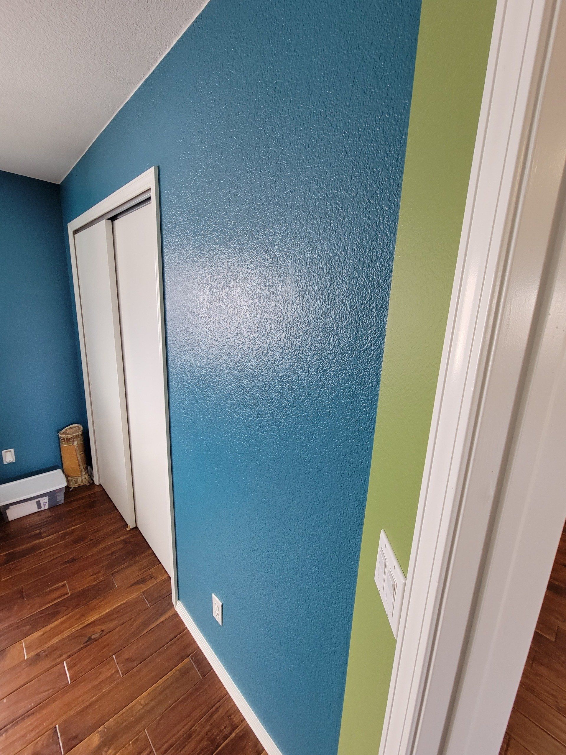 A hallway with blue and green walls and a wooden floor.