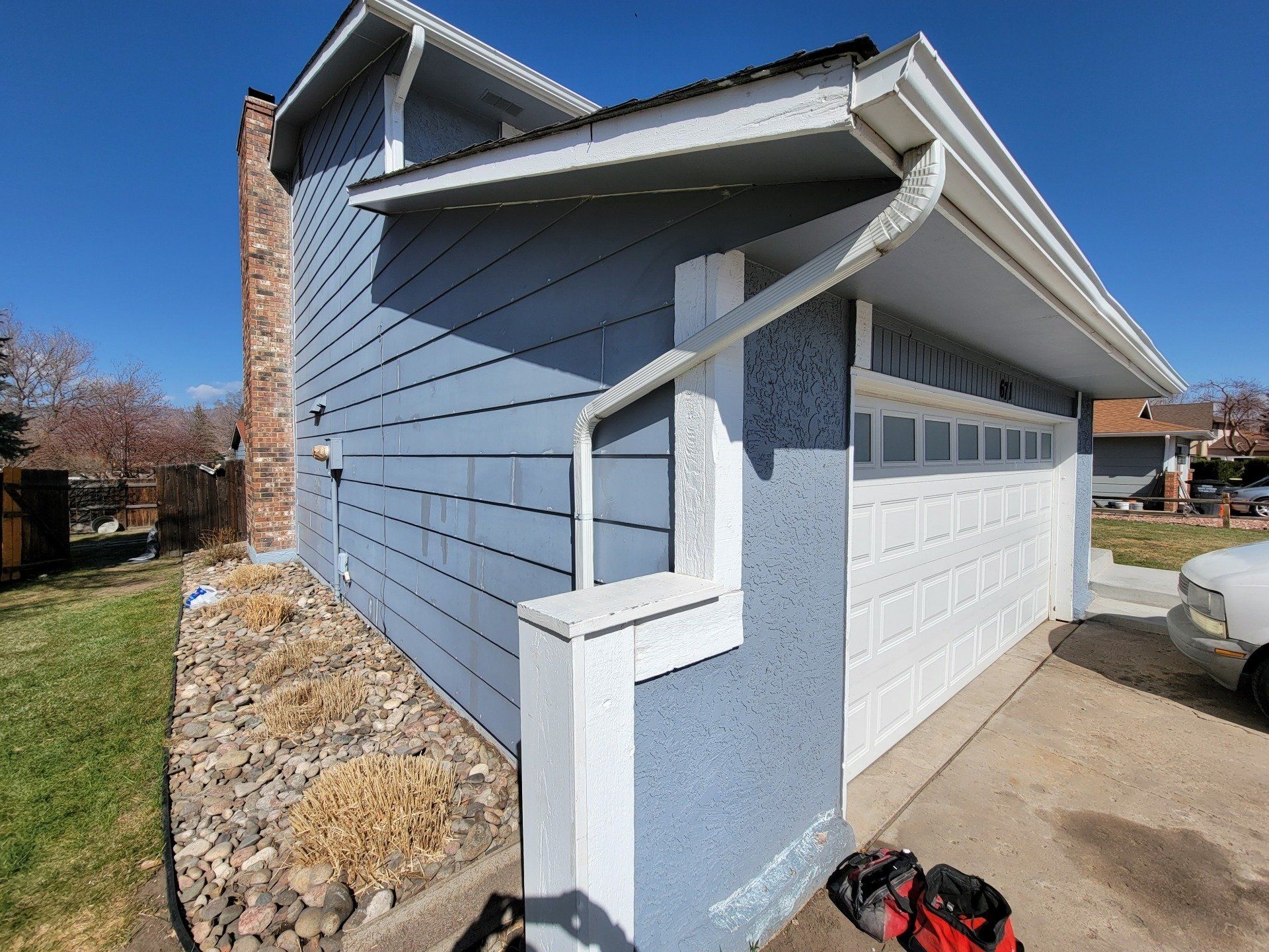 A white truck is parked in front of a blue house with a white garage door.