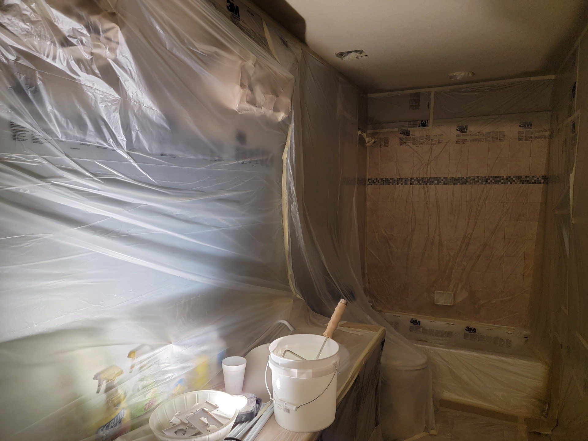 A bathroom with a bucket of paint and a brush on the counter.