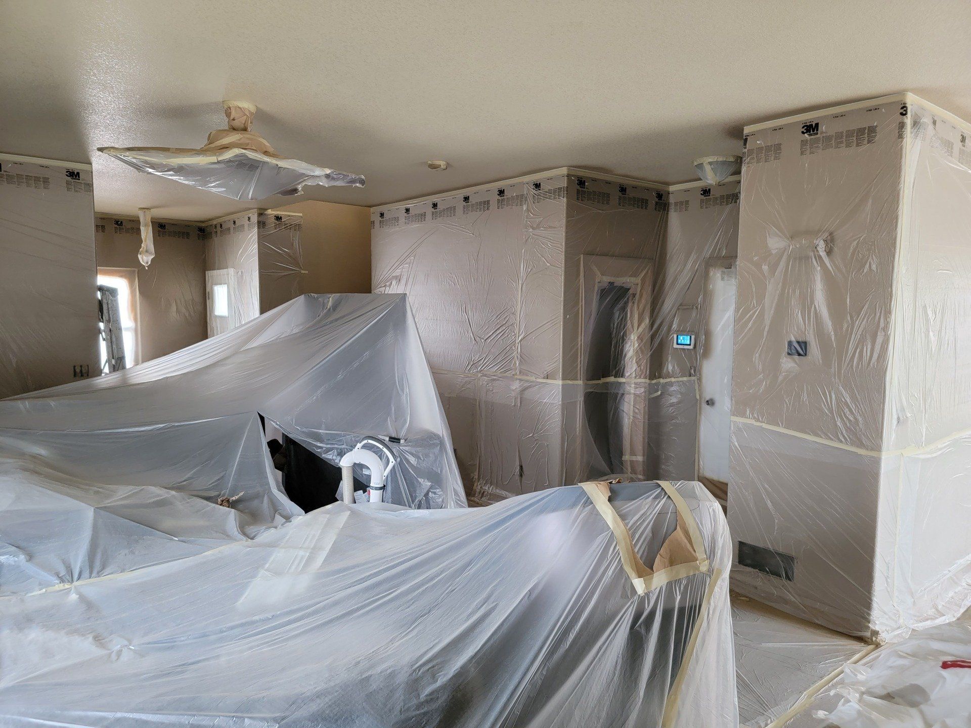 A living room is being painted and covered in plastic.