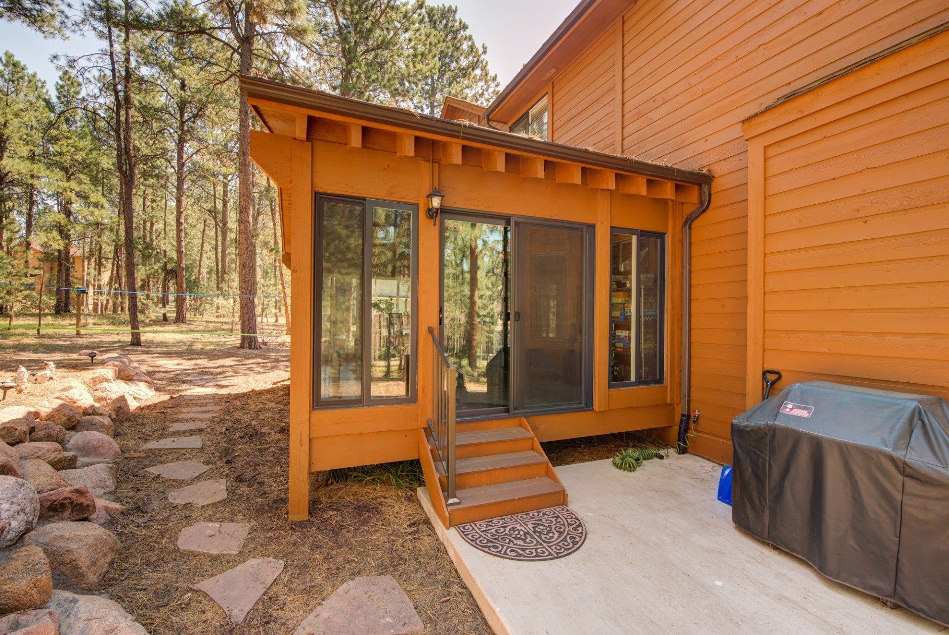A wooden house with a patio and a grill in front of it.