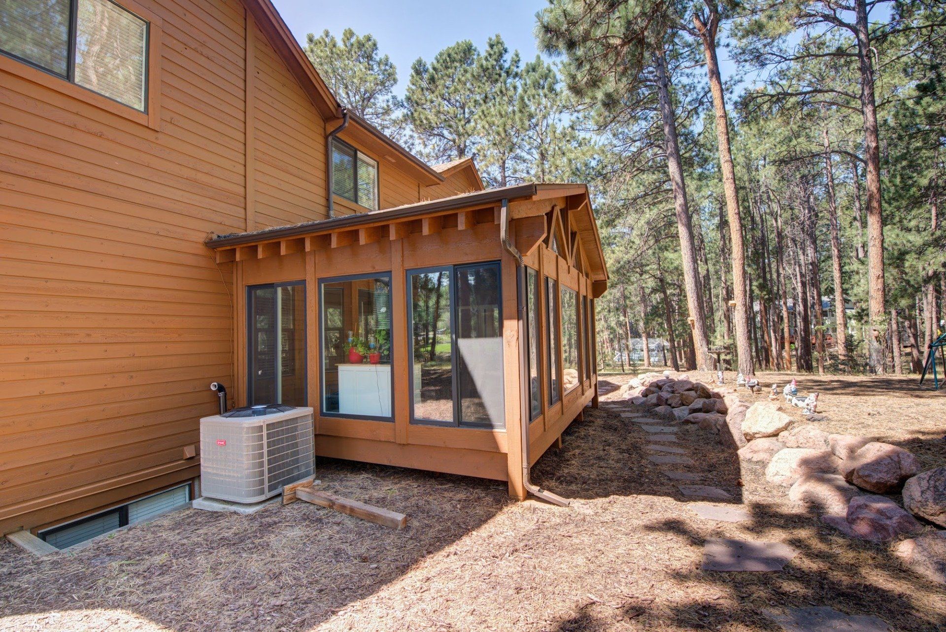 A large wooden house with a large sun room in the backyard surrounded by trees.