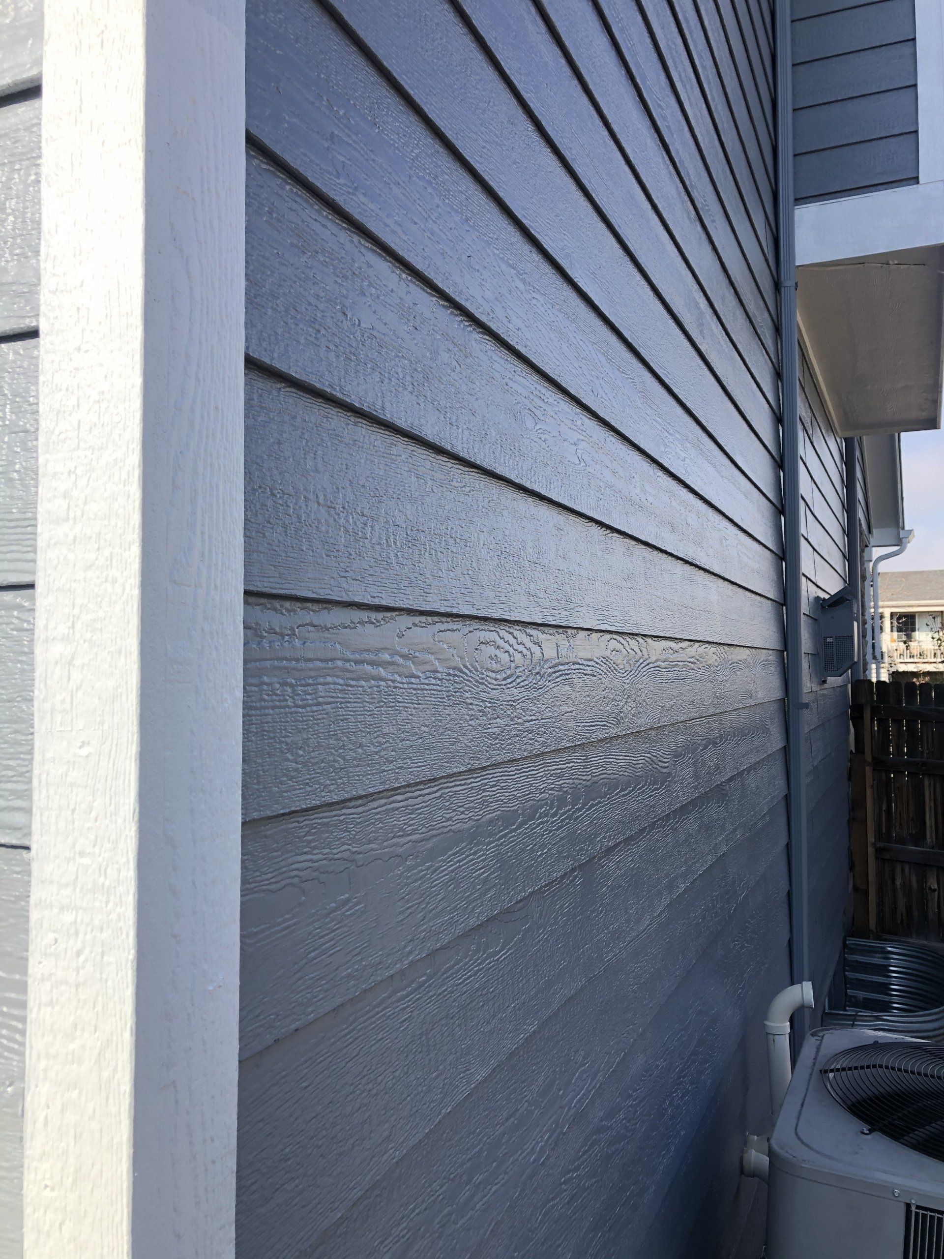 The side of a house with a gray siding and a white trim.