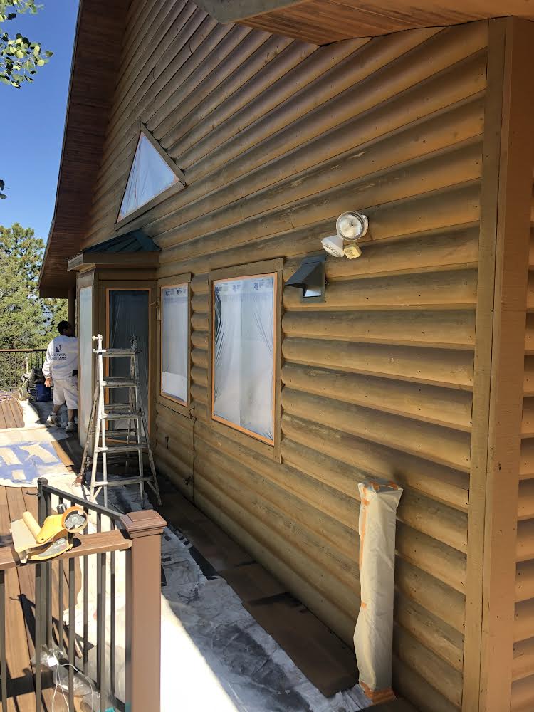 A log cabin is being painted on a sunny day.