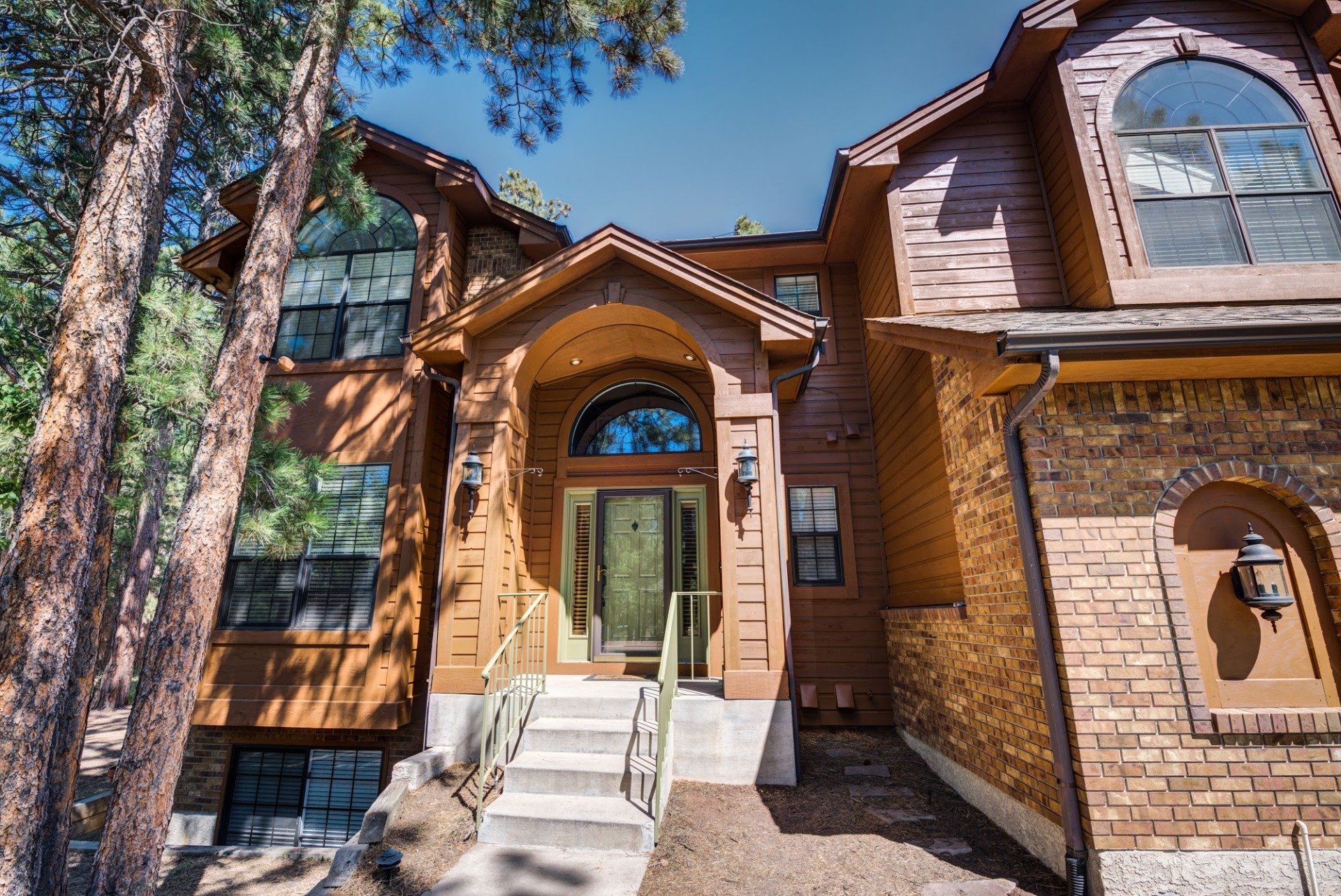 A large wooden house with stairs leading up to the front door surrounded by trees.