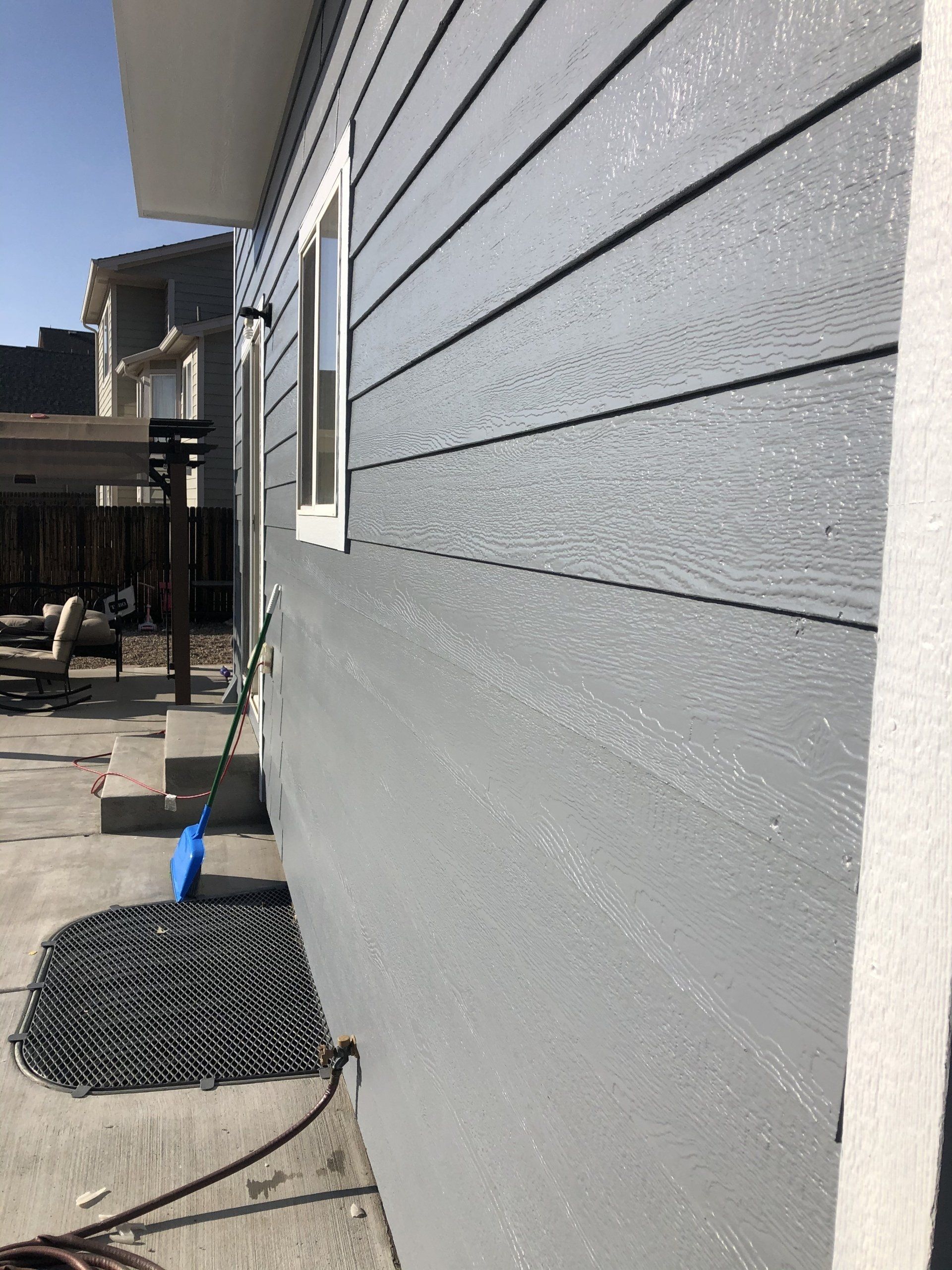 A gray house with a window and a hose on the side of it.