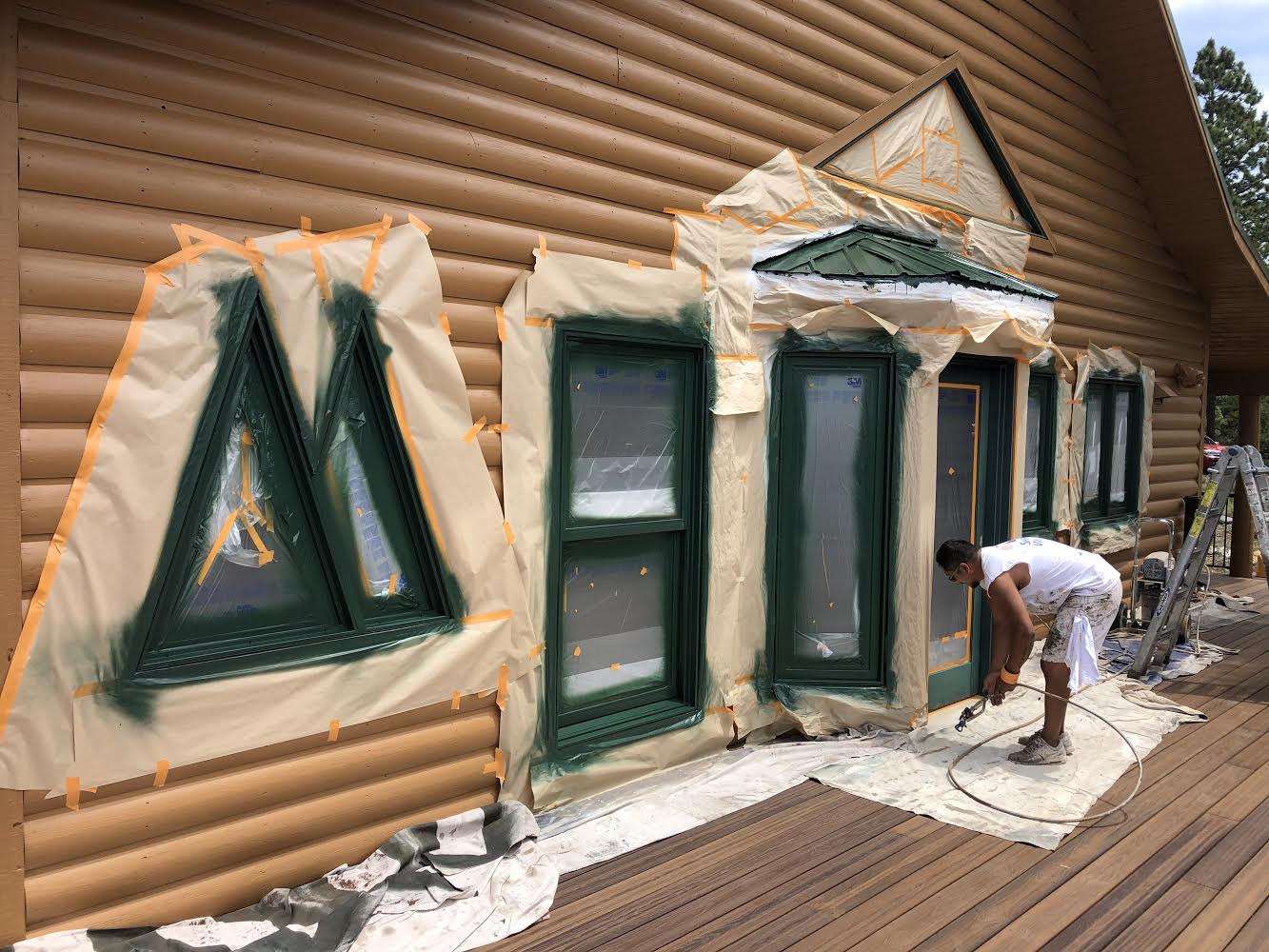 A man is painting the outside of a log cabin.