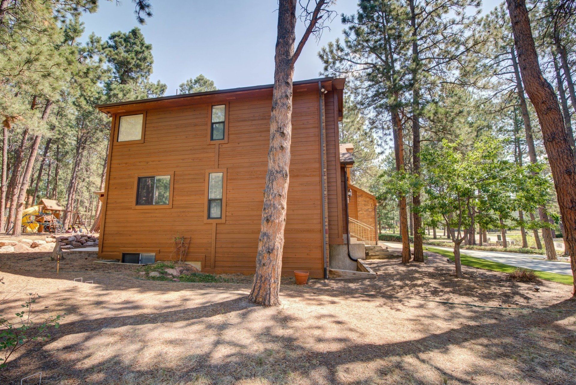 A large wooden house is surrounded by trees in the middle of a forest.