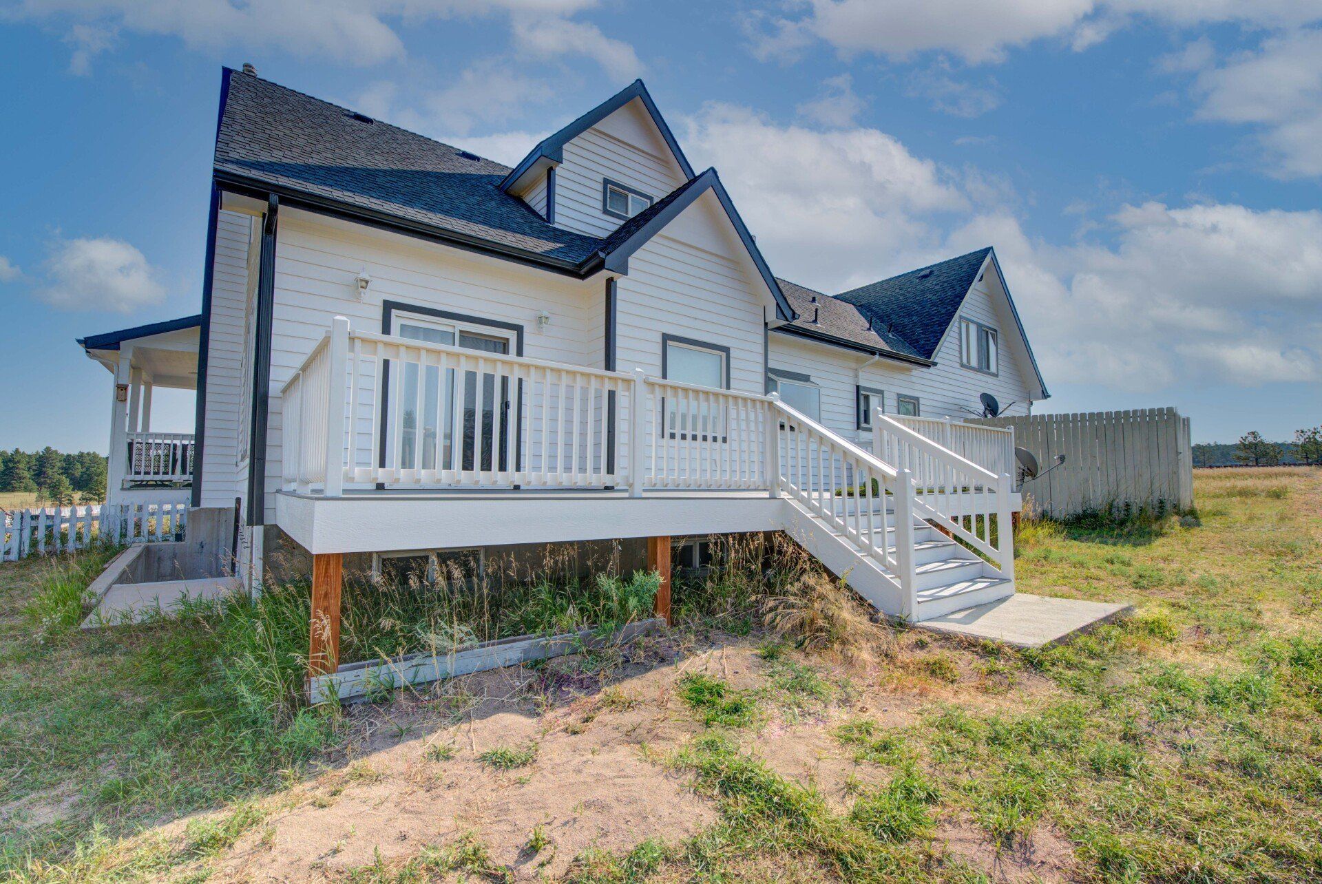 A white house with a large deck and stairs leading up to it.
