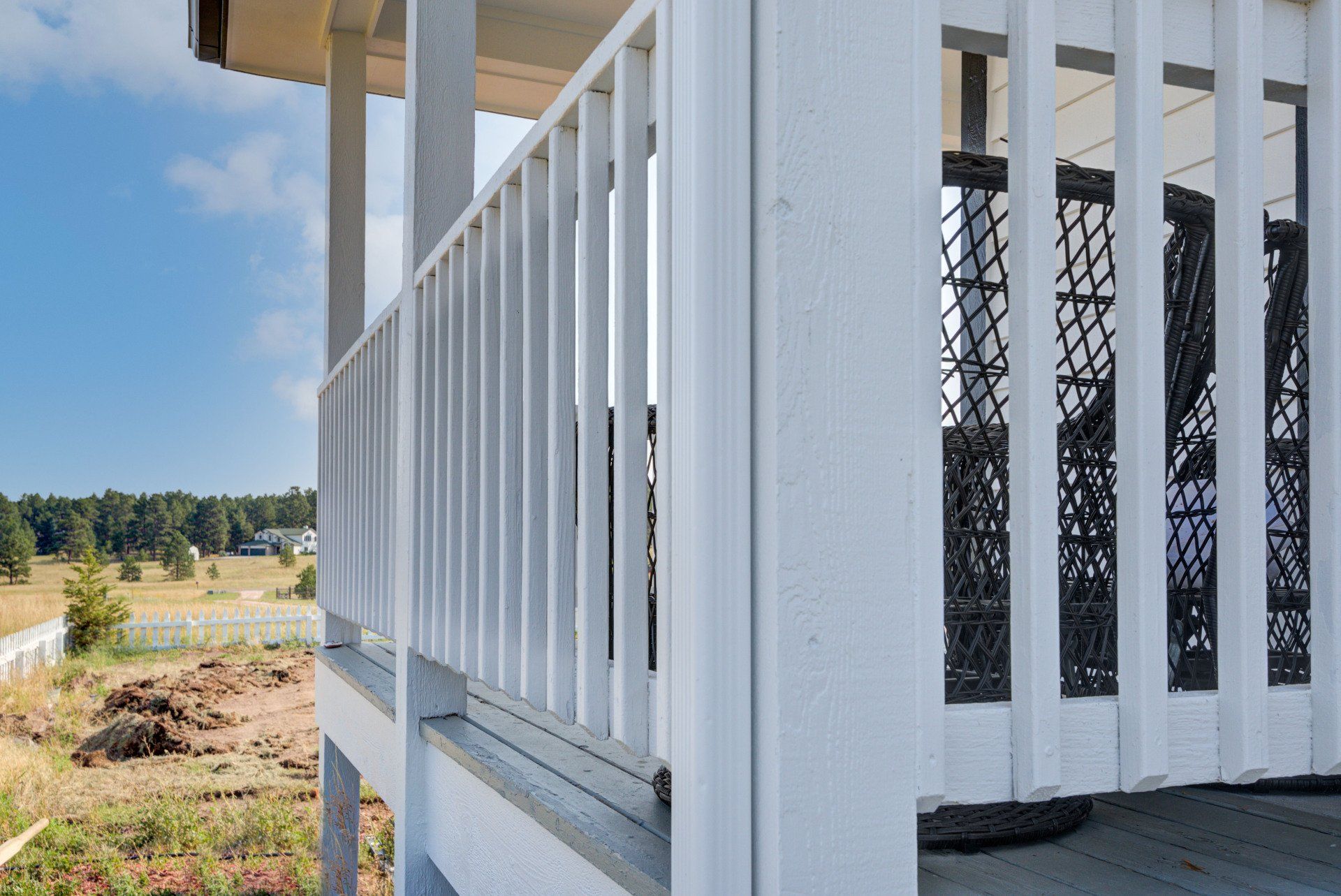 A white railing on a porch with a view of a field