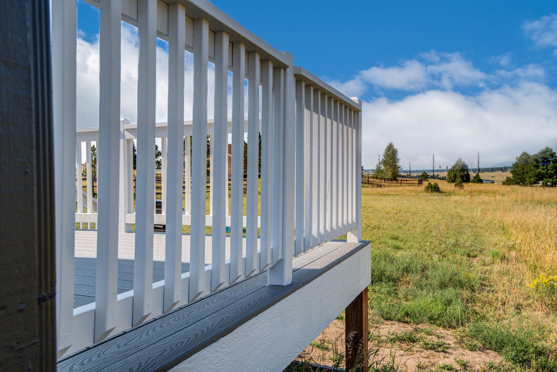 A white railing on a deck overlooking a grassy field.